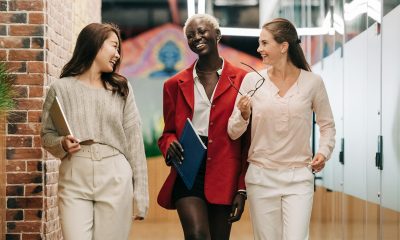 Group of young glad businesswomen in trendy elegant outfits smiling and discussing business strategy in contemporary workspace