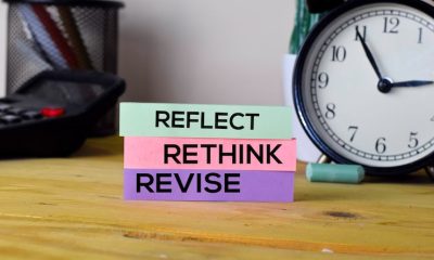 Reflect, Rethink, Revise sticky notes on desk with clock, promoting self-improvement and time management strategy