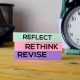Reflect, Rethink, Revise sticky notes on desk with clock, promoting self-improvement and time management strategy