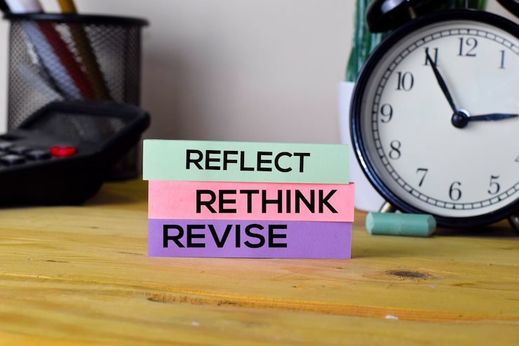 Reflect, Rethink, Revise sticky notes on desk with clock, promoting self-improvement and time management strategy