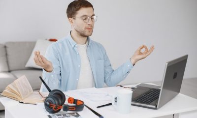 Man practising mindfulness meditation at his desk with a laptop, notebook, and headphones in a home office setting
