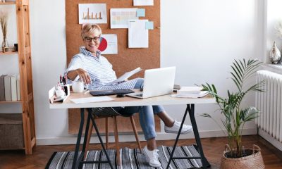 Woman working at a stylish home office desk with a laptop, papers, and corkboard with charts