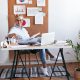 Woman working at a stylish home office desk with a laptop, papers, and corkboard with charts