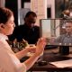 Person on video call in modern office setting, collaborating with colleagues at desk with paperwork and computer