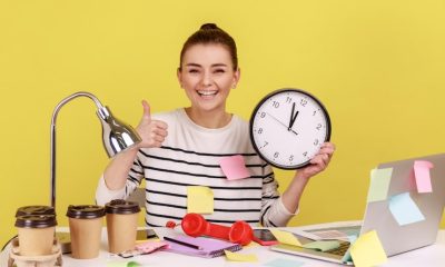 Person smiling and holding a clock, surrounded by sticky notes, coffee cups, and office items on a yellow background