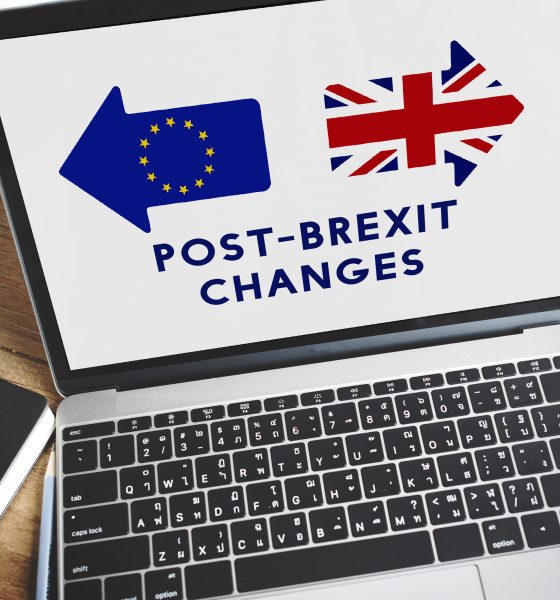 Laptop displaying EU and UK flags with text 'Post-Brexit Changes', beside coffee and notebook on wooden desk
