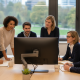 Diverse team engaged in a collaborative office meeting, reviewing a computer monitor's display, notes on table